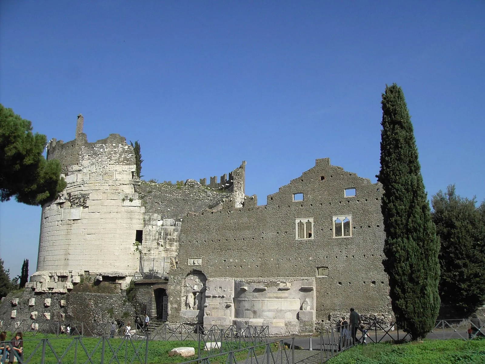 Il Mausoleo di Cecilia Metella sulla Via Appia Antica, con la torre cilindrica in travertino e le mura merlate del castello medievale, tra pini e cipressi