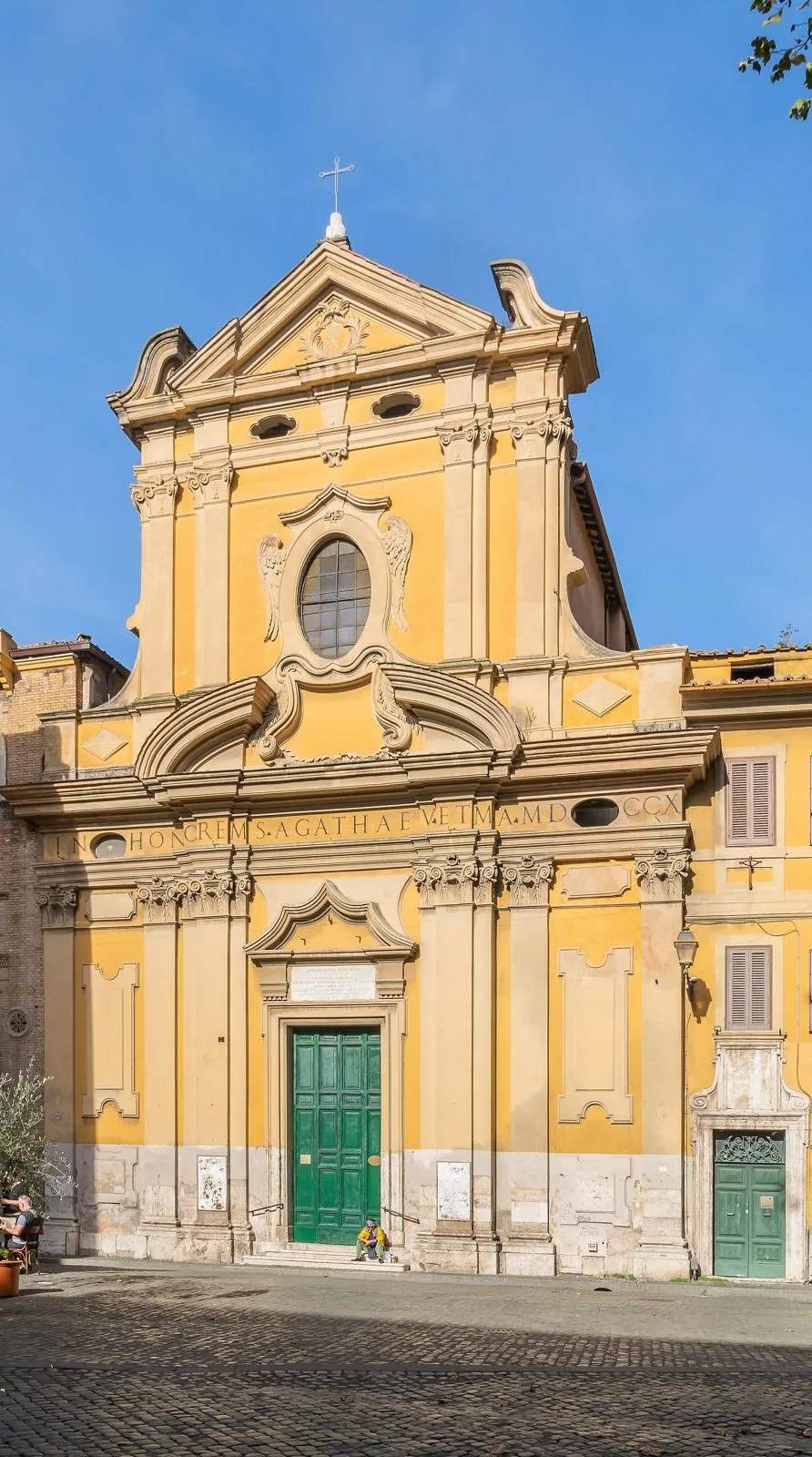 Facciata barocca gialla della chiesa di Sant'Agata in Trastevere, con portone verde, sotto il cielo azzurro